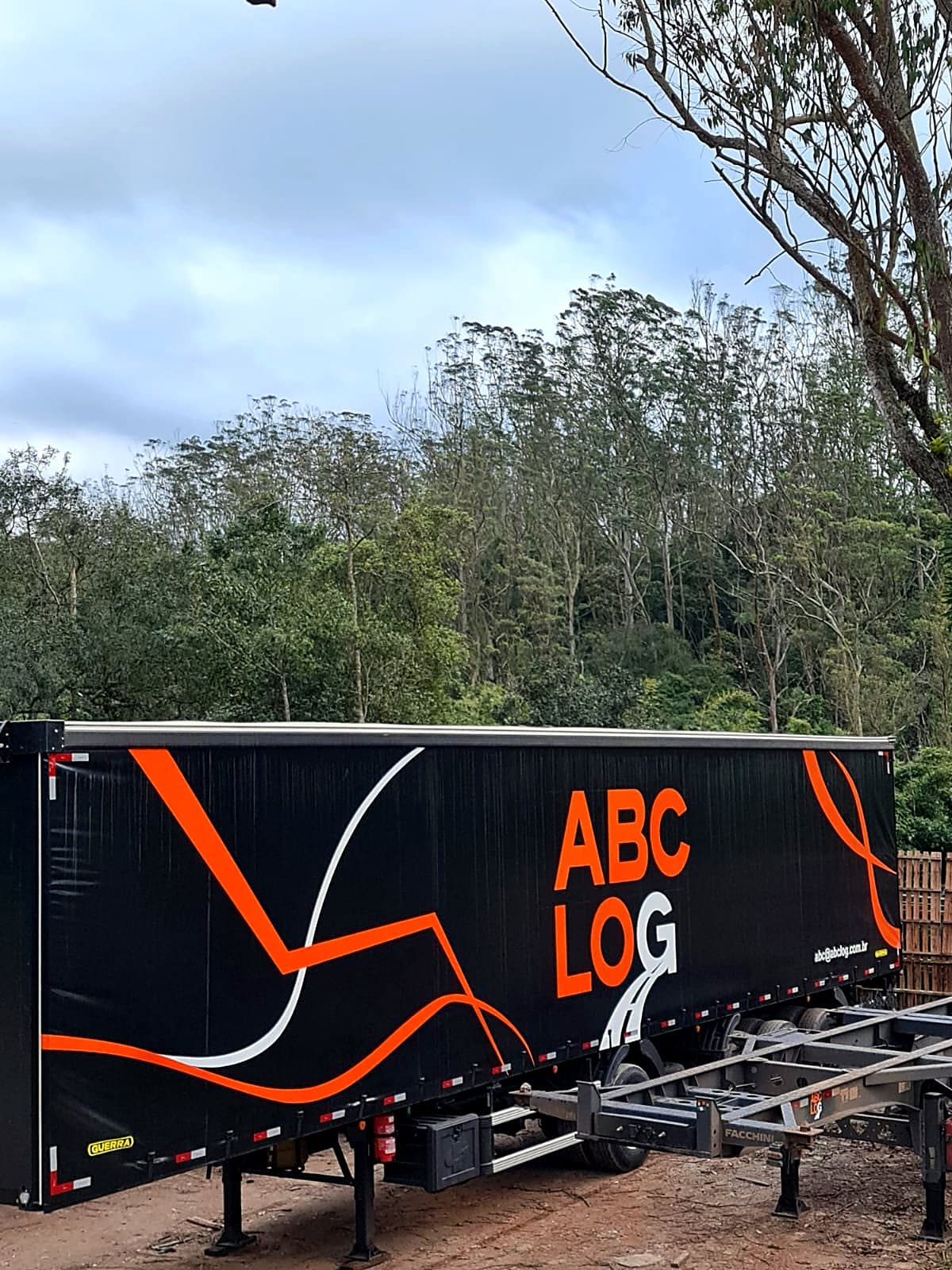 Carreta sider preta da ABC Log com linhas laranja e brancas pintadas na lona, ao ar livre