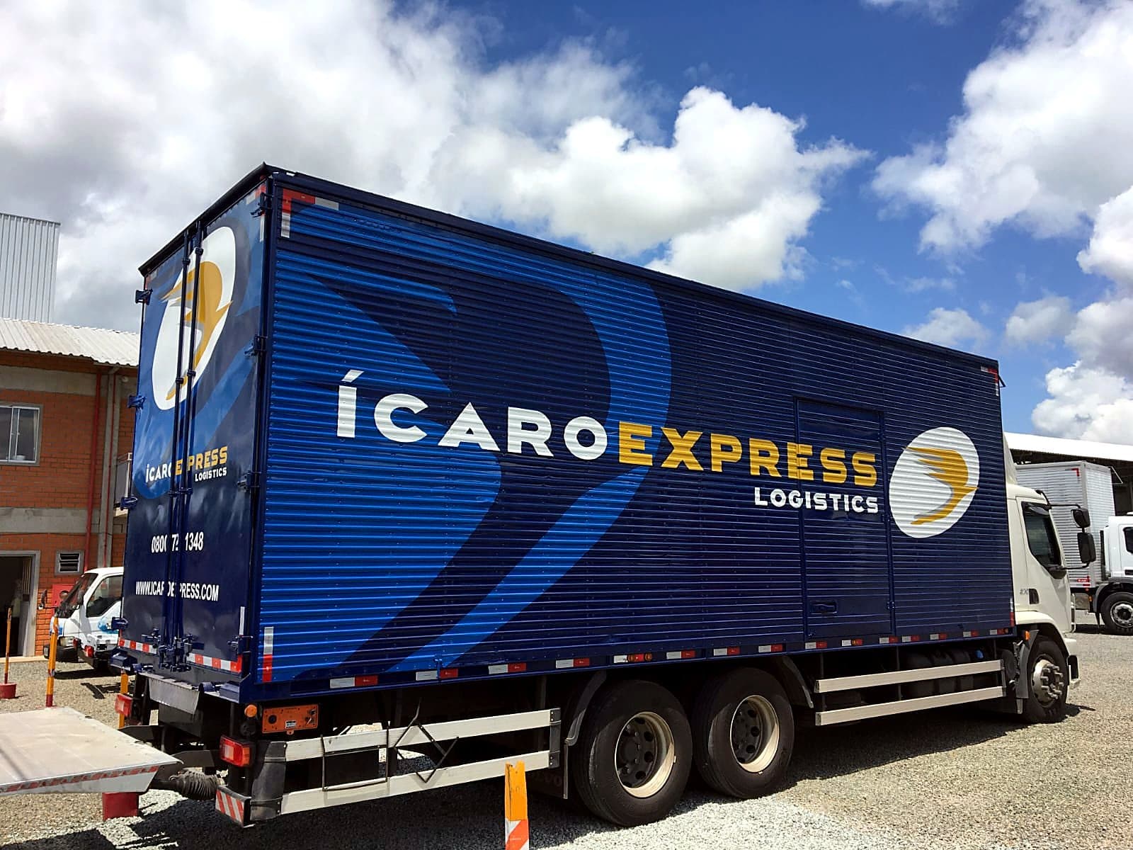 Caminhão baú azul da Ícaro Express com logomarca e grandes grafismos pintados, sob céu azul