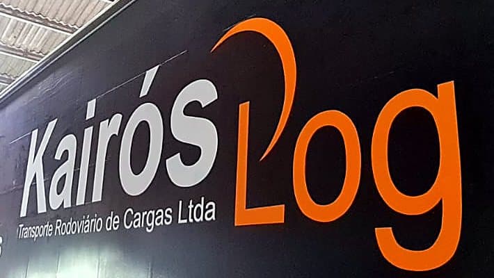Detalhe da logomarca Kairós Log em branco e laranja pintada na lona preta