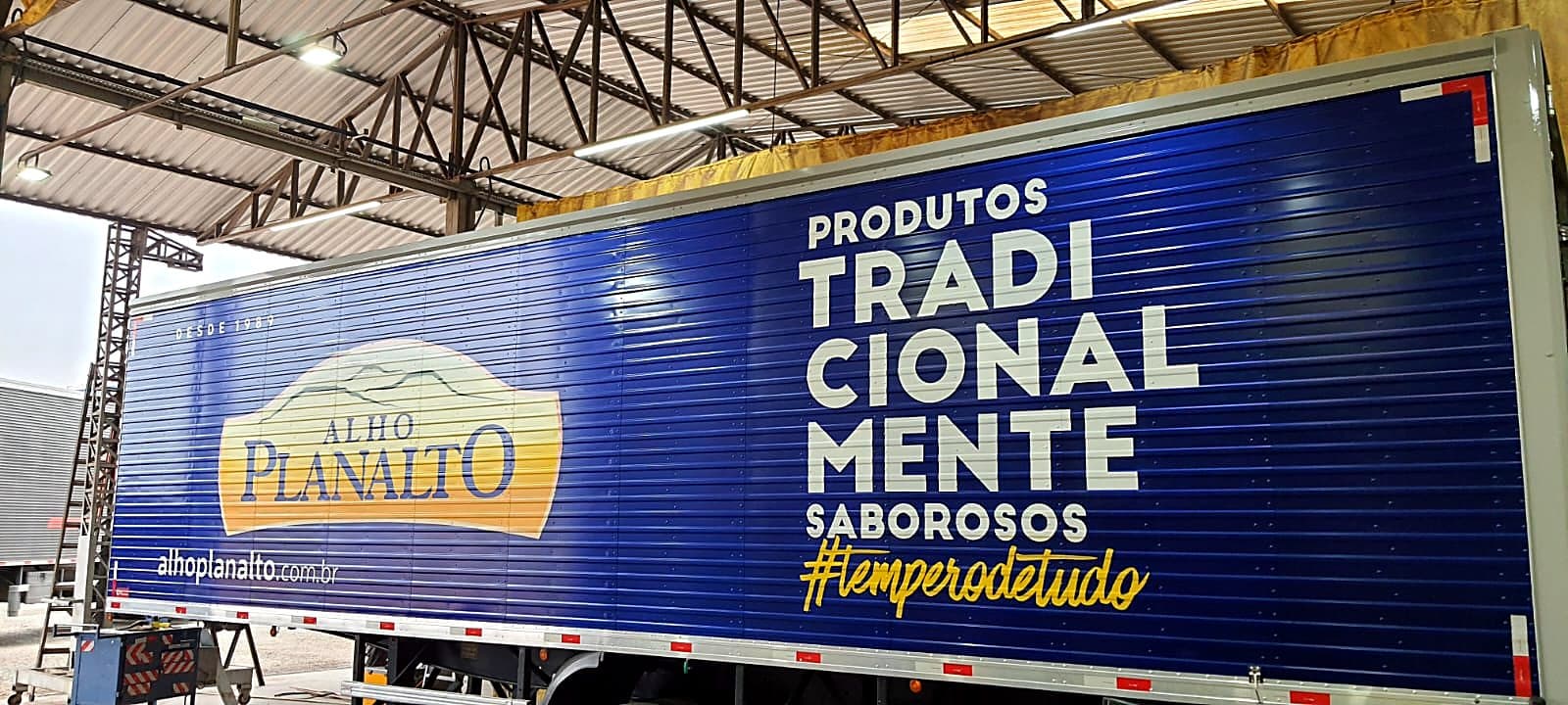 Semirreboque baú azul da Alho Planalto com logomarca, slogan e assinatura cursiva