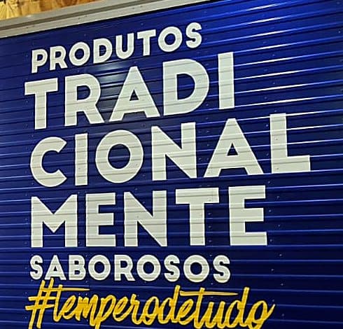 Detalhe do slogan em letras brancas grandes e da assinatura cursiva amarela da Alho Planalto